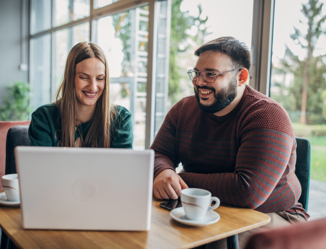 Un homme et une femme assis dans un café devant un ordinateur